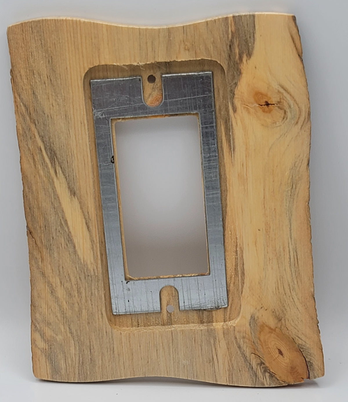 A rustic, handcrafted wooden wall plate or decorative frame with a live edge, featuring a central cutout containing a brushed silver metal plate cutout in the center for toggle light switch.
