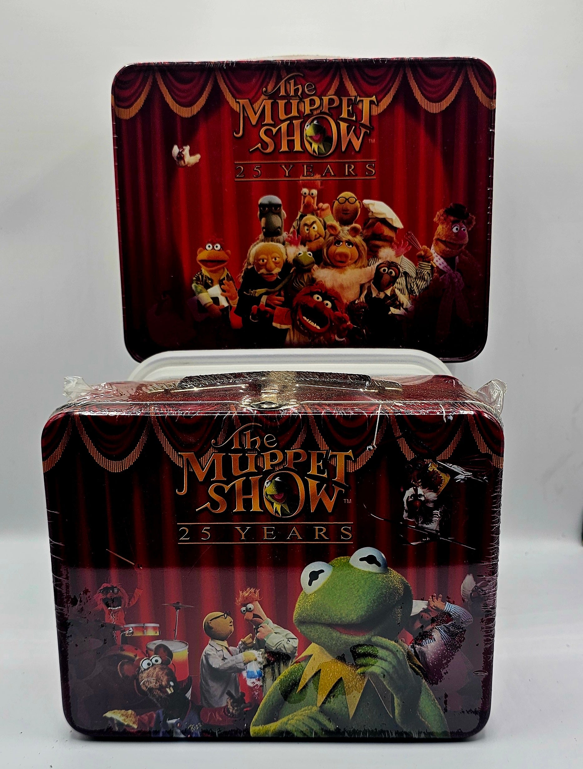 A collectible metal tin featuring 'The Muppet Show 25 Years' with Kermit the Frog on the front and a group of Muppets on the lid, sealed in clear plastic wrap against a light gray background.