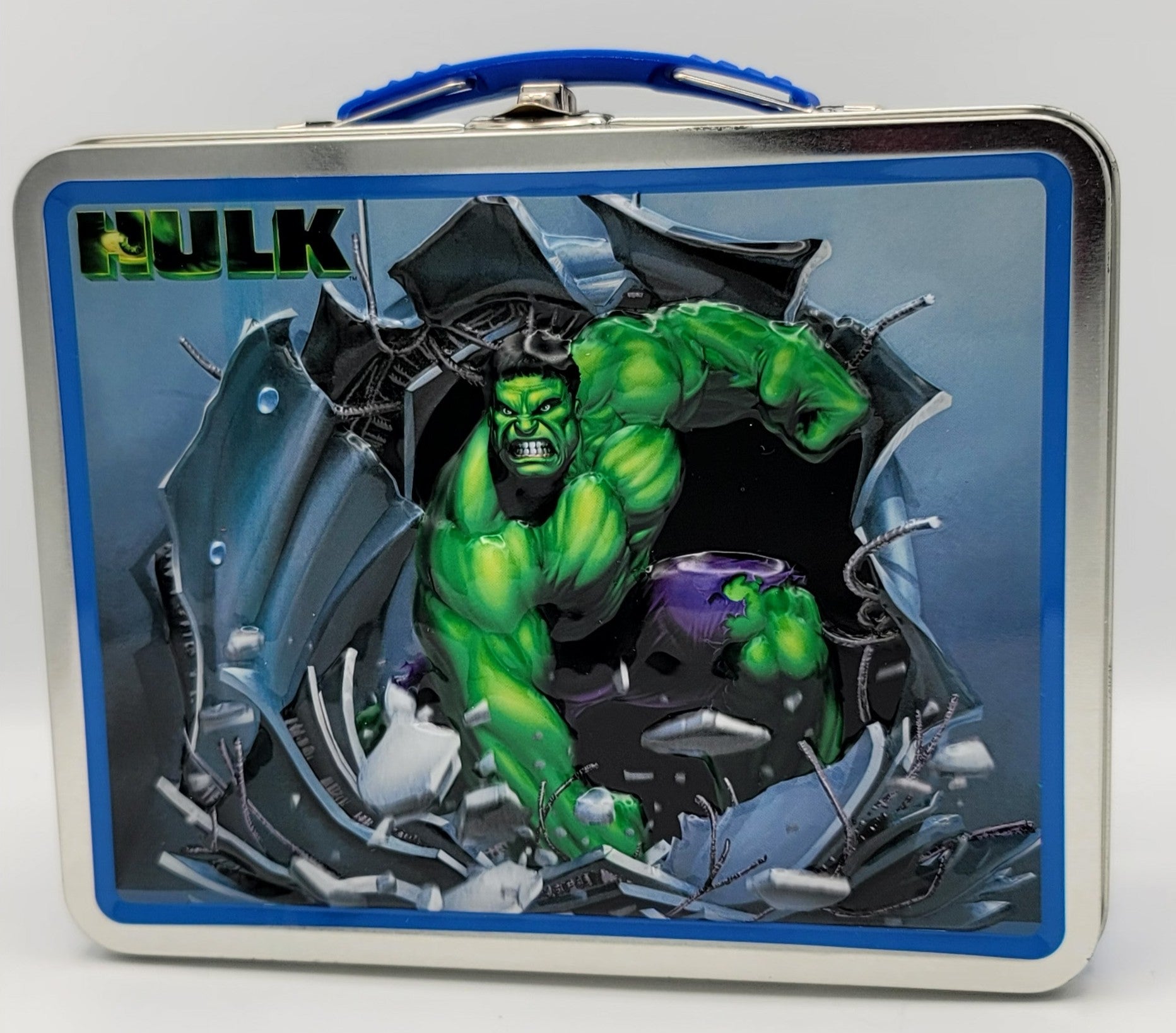 The glossy blue metal side panel is beautifully detailed with a vertical column of three retro-styled, yellow and purple atomic biohazard radiation symbols linked together by a continuous white jagged energy soundwave graphic. The front cover of the tin is visible at a sharp angle, showcasing the bright chrome edge trim and the embossed 3-D graphic of the Incredible Hulk busting through the wall next to the blocky green "HULK" logo. A matching blue plastic handle sits centered on the silver latch mechanism