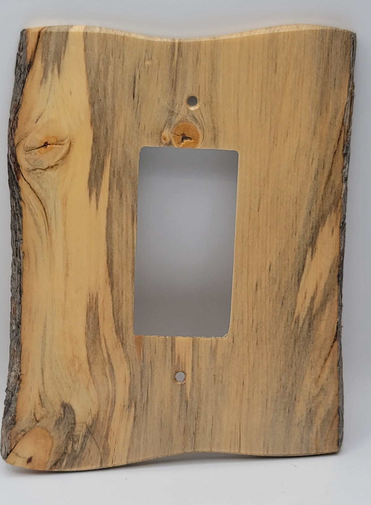 A rustic light switch plate cover made from a live-edge wood slab, featuring natural grain patterns and bark on the sides, with a rectangular cutout in the center for toggle light switch.