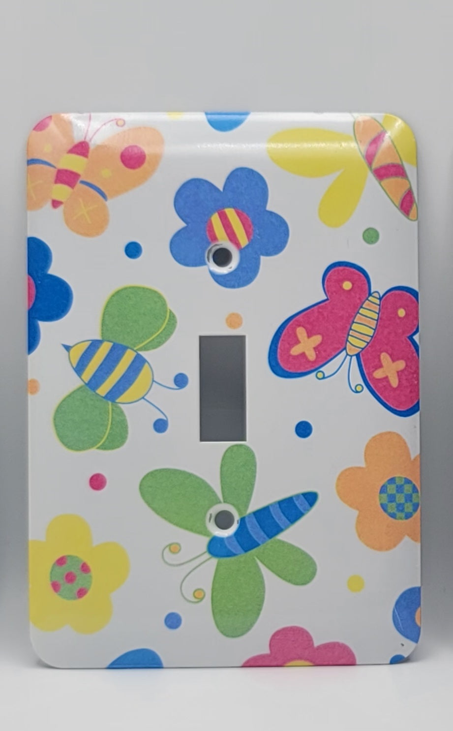 A single-toggle light switch plate cover decorated with a colorful cartoon butterfly, bee, dragonfly, flower, and dot pattern on a white background.