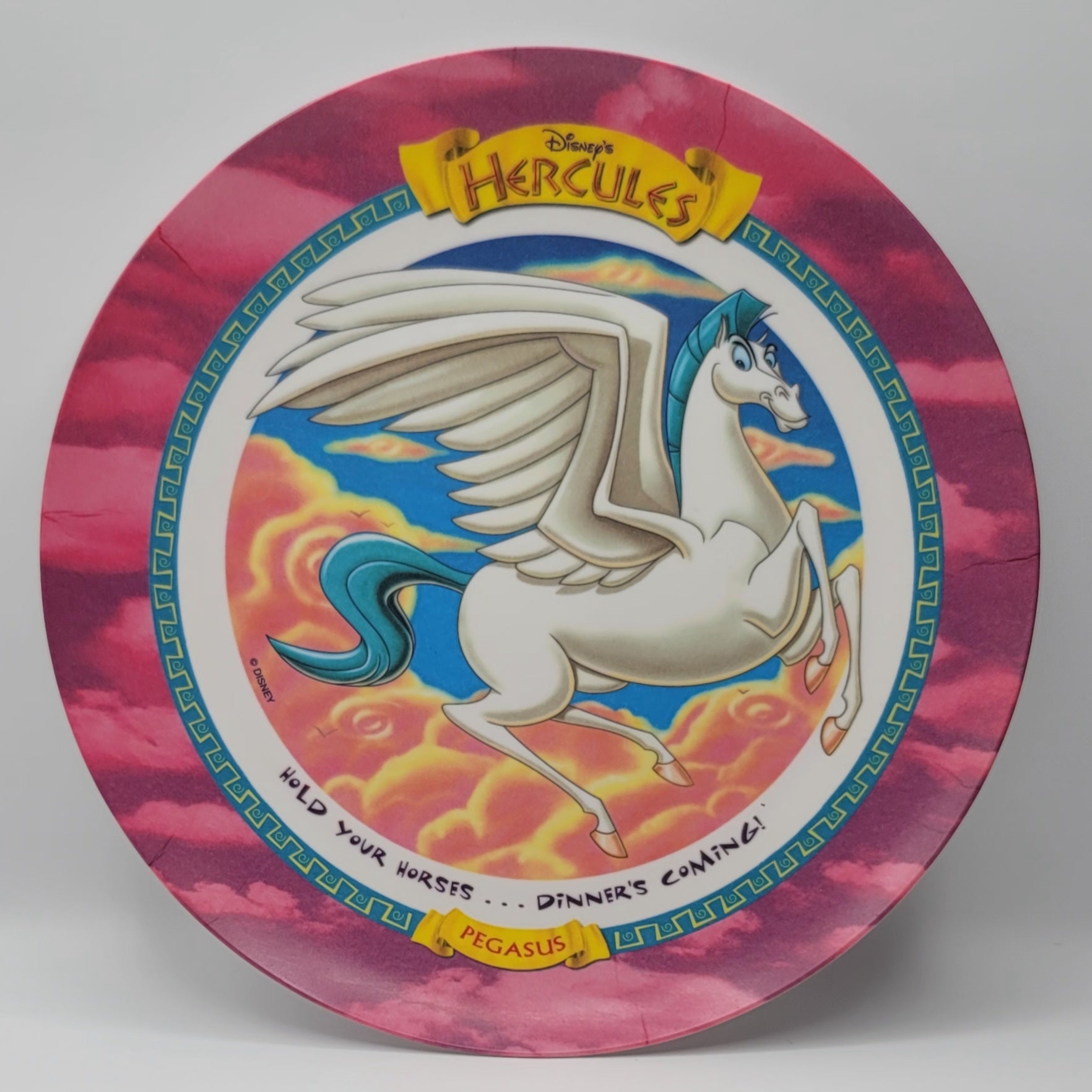 Disney's Hercules Pegasus collectible ceramic plate featuring an illustration of the white winged horse Pegasus with a blue tail and mane, set against a pink and purple cloud-patterned border with yellow banner accents.