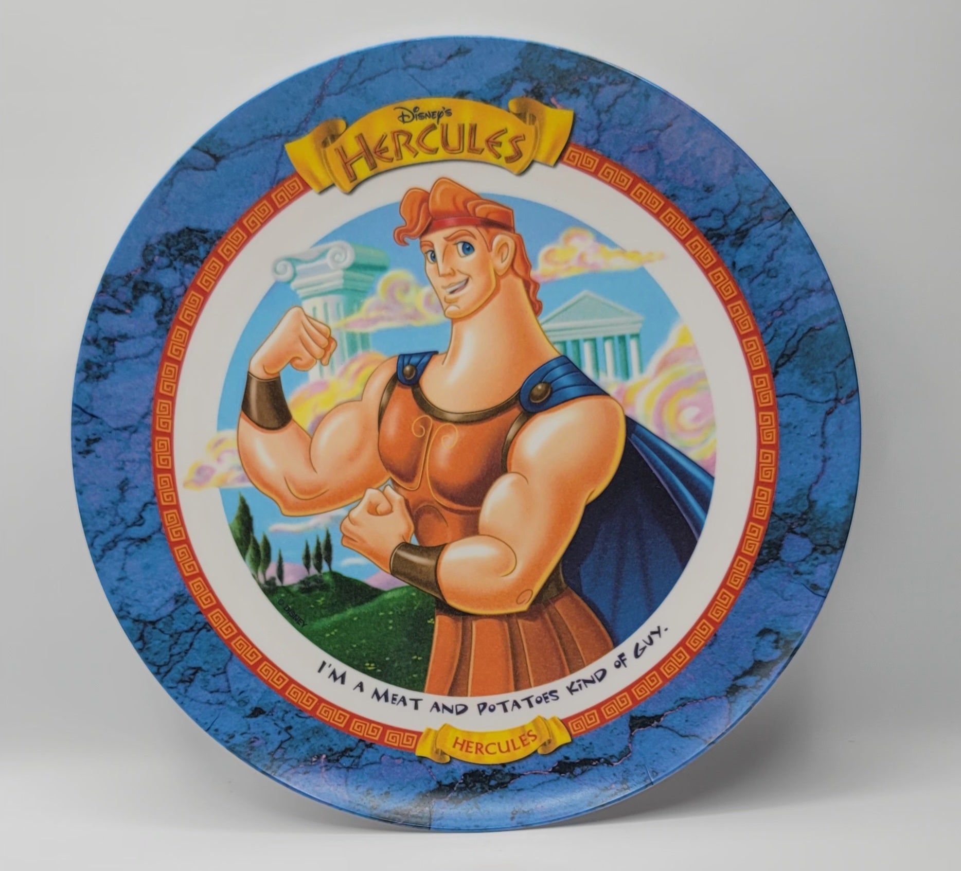 Disney's Hercules collectible ceramic plate featuring a colorful illustration of the character with his signature red hair, muscular physique, and blue cape against a blue marble-textured background.