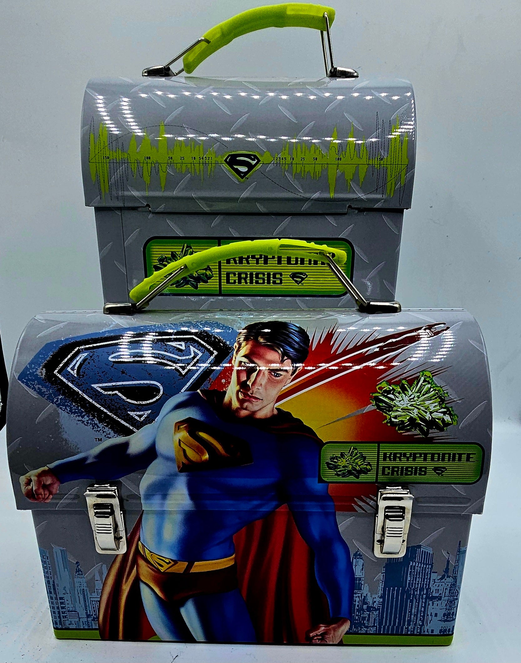 A Superman-themed metal lunch box set with a smaller top box and a larger bottom box, both in gray with bright green handles and graphics, featuring Superman and the words 'Kryptonite Crisis'.