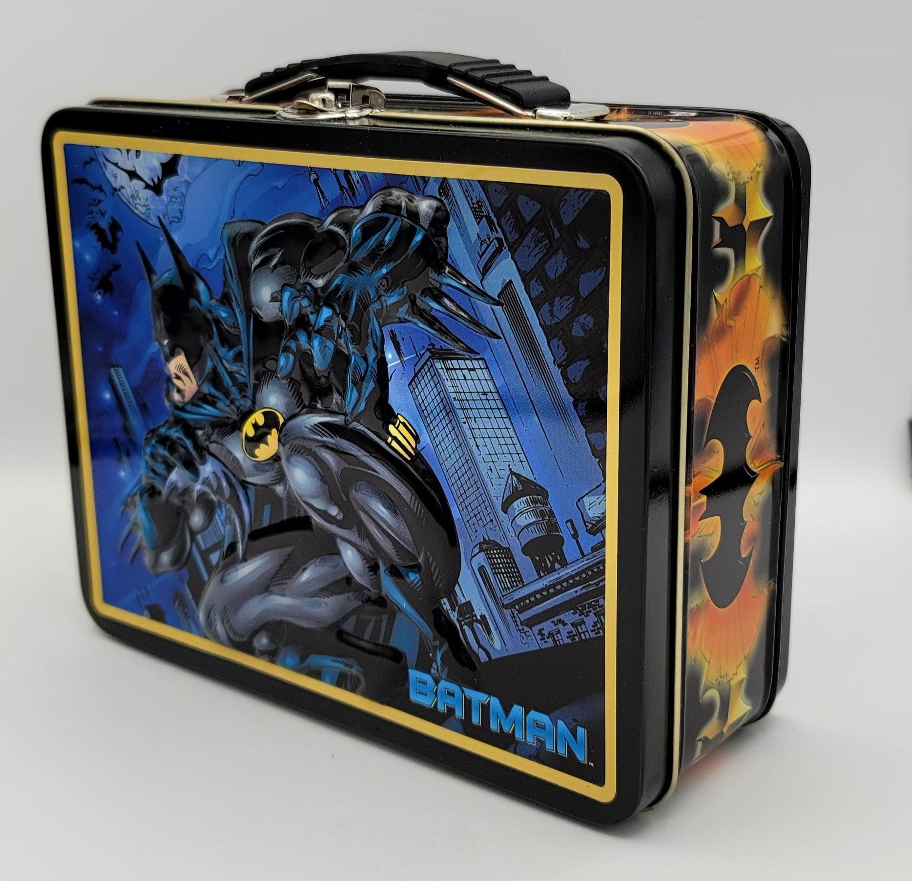 A vintage-style metal lunch box featuring Batman artwork on the front and side panels, with a black handle and silver latch, photographed on a light gray background.