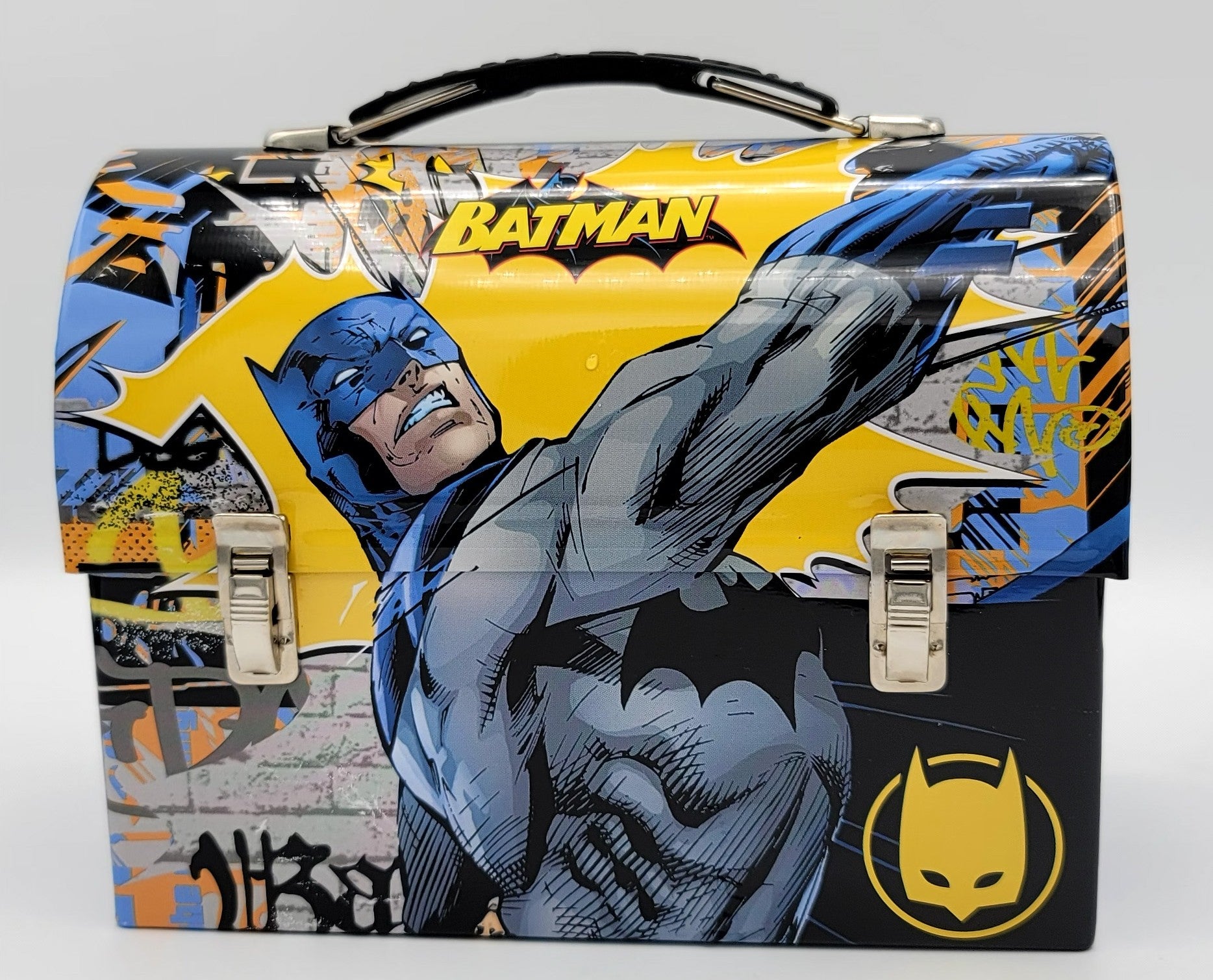 A Batman-themed metal lunch box featuring a dynamic comic-style illustration of Batman in blue and gray, with a bright yellow background, graffiti elements, and silver latch closures on the front.