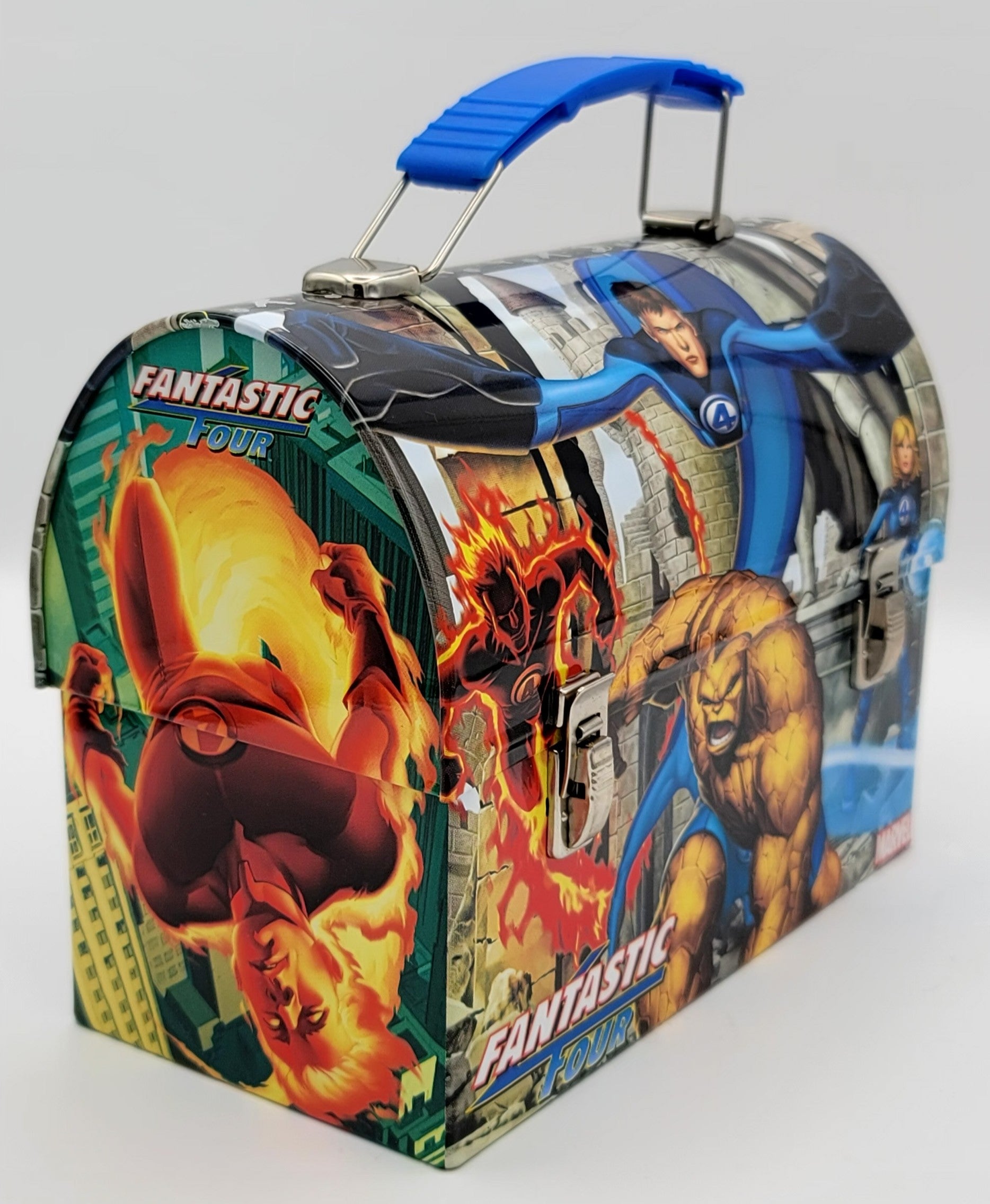 A Fantastic Four themed metal lunch box featuring printed comic book artwork of the characters with a blue plastic handle, photographed on a light gray background.