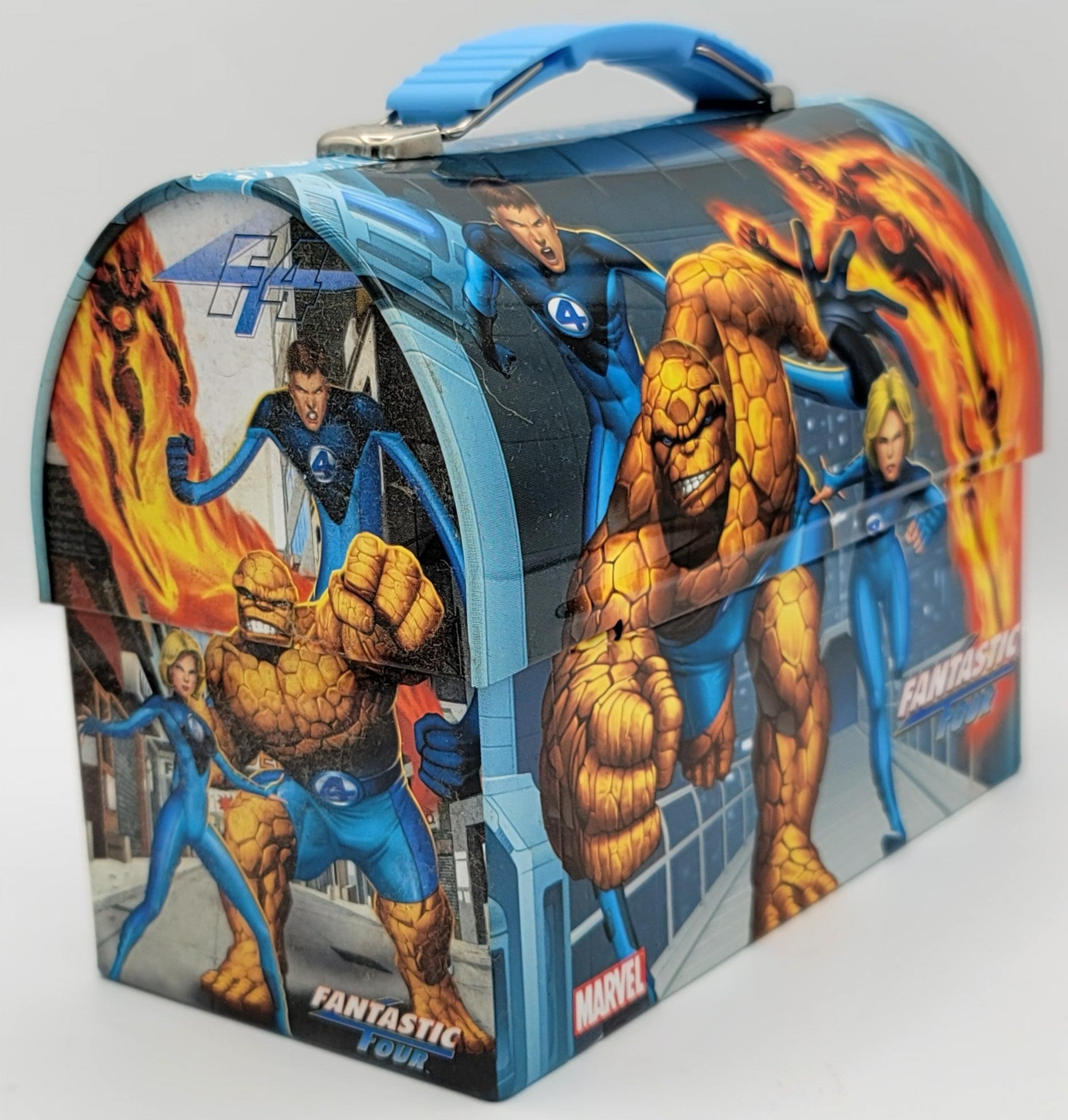 A Marvel Fantastic Four themed lunch box featuring illustrated depictions of the four heroes, including the Thing, Invisible Woman, Human Torch, and Captain America, with a blue handle on a light gray background.